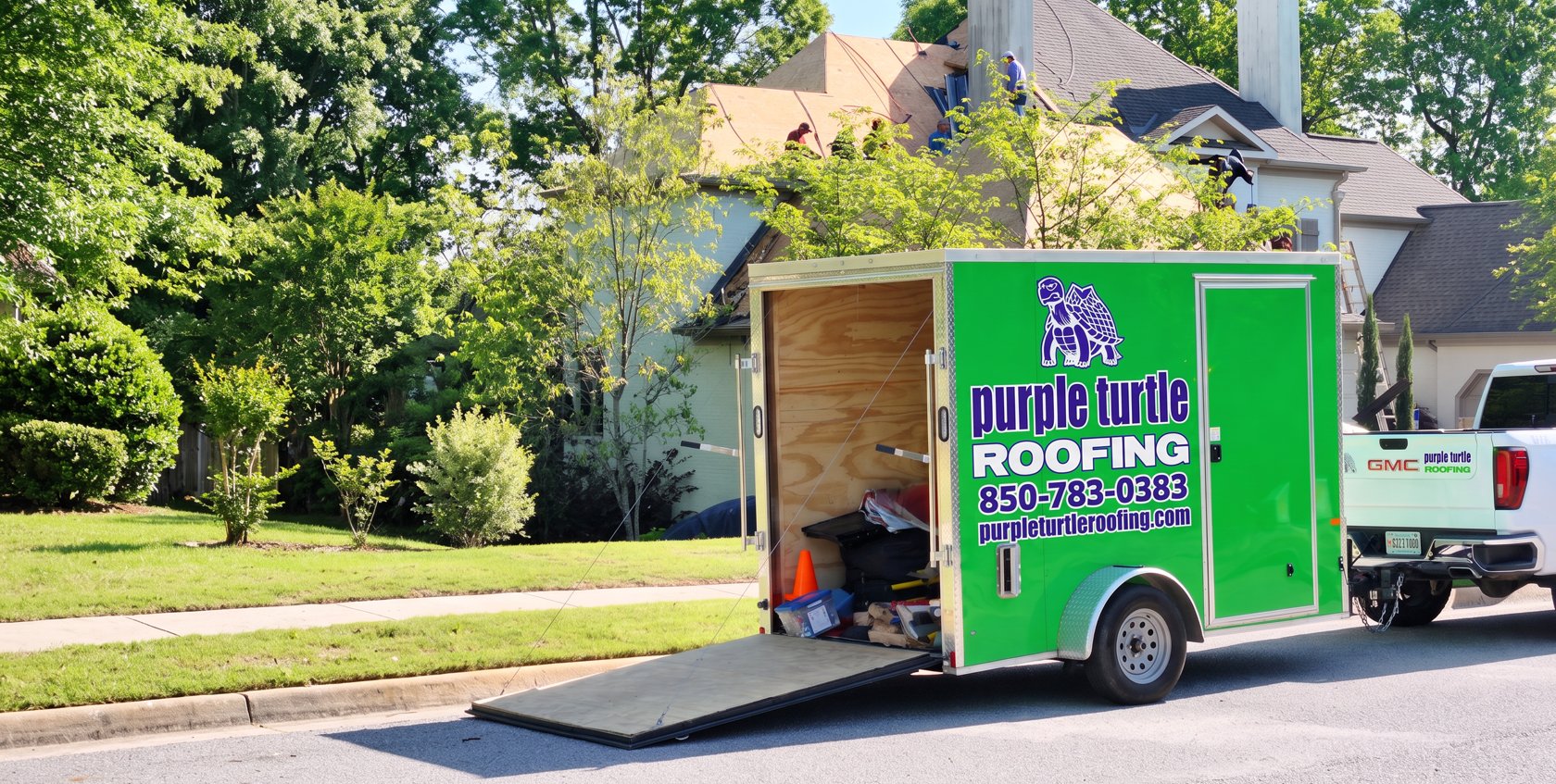 Purple Turtle Roofing truck and branded trailer parked in front of a Fort Walton Beach home with its roof stripped for replacement, crew working on the roof, phone number 850-783-0383 on the trailer